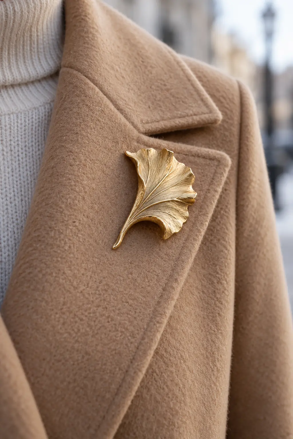 Brushed-gold leaf brooch pinned high on the supported lapel of a camel wool coat