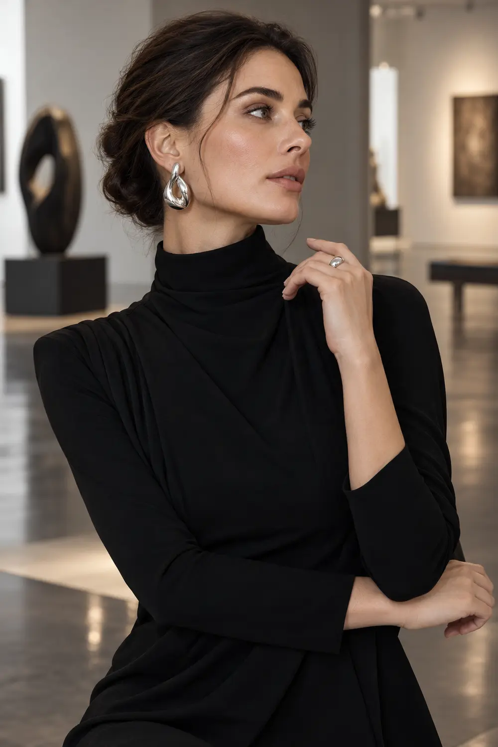 Woman in a black high-neck dress wearing sculptural silver statement earrings